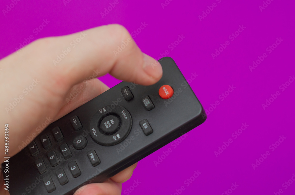 remote control in hand with red button on purple background remote control in hand with red button on purple background