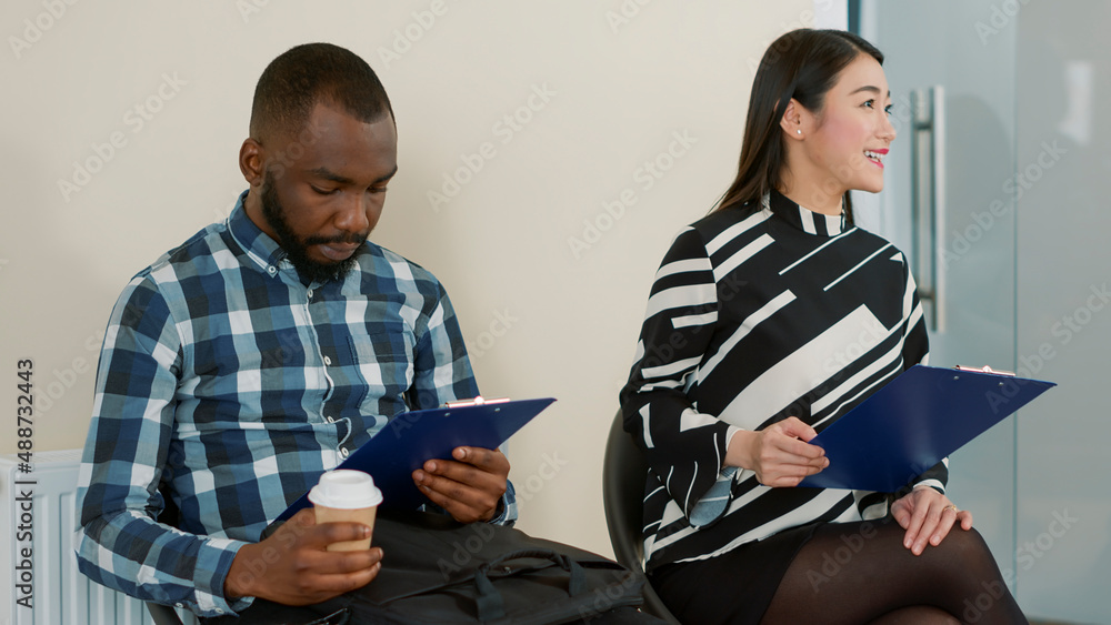 Multiethnic group of people waiting in queue at job interview, reading recruitment papers in lobby. Man and woman preparing to attend employment meeting for business career opportunity. Multiethnic group of people waiting in queue at job interview, reading recruitment papers in lobby. Man and woman preparing to attend employment meeting for business career opportunity.