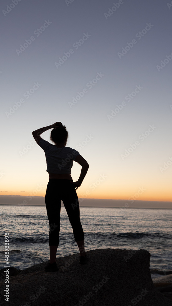 Lady's silhouette with raised arm against calm sunset beach