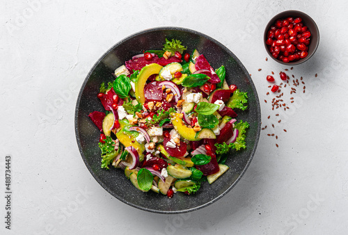 Healthy vegetarian vegetable salad with beetroot, avocado, feta and pomegranate on a gray background.