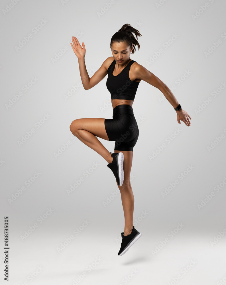 Side view of athletic female model jumping by white color background, warm-up before workout and jogging