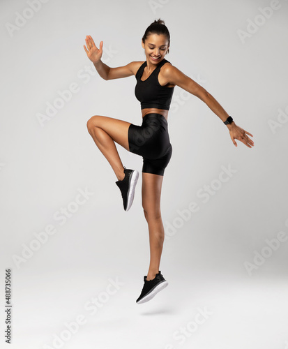 Side view of athletic female model jumping by white color background, warm-up before workout and jogging