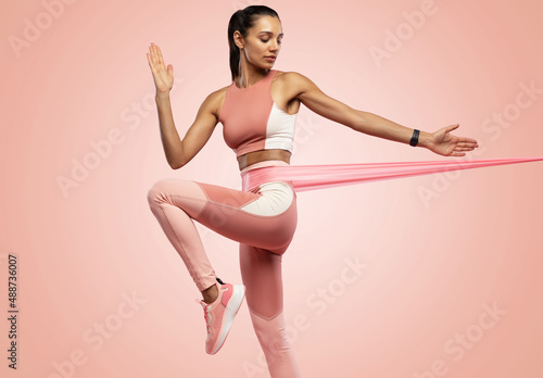 Sportswoman exercising with resistance band. Female with working out with elastic band on pink background photo