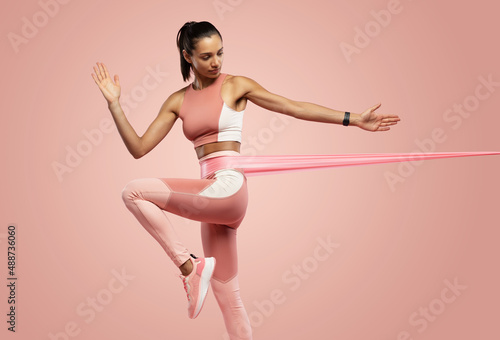 Sportswoman exercising with resistance band. Female with working out with elastic band on pink background