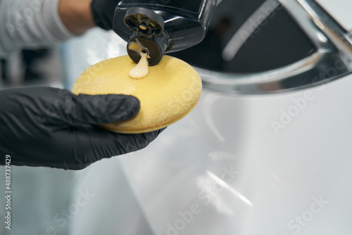 Gloved hands applying liquid wax on foam sponge
