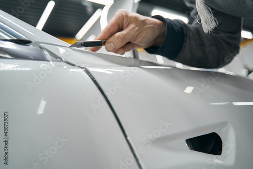 Professional auto detailer removing extra PPF coating from automobile