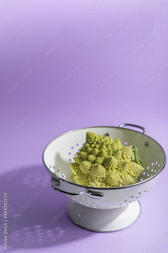 Romanesco cabbage in a white colander on a purple background. BIO-Vegetables. Romanesco cabbage in a white colander on a purple background. BIO-Vegetables.