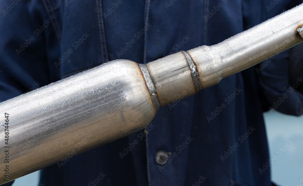 part of a muffler for a car in the hands of a car mechanic