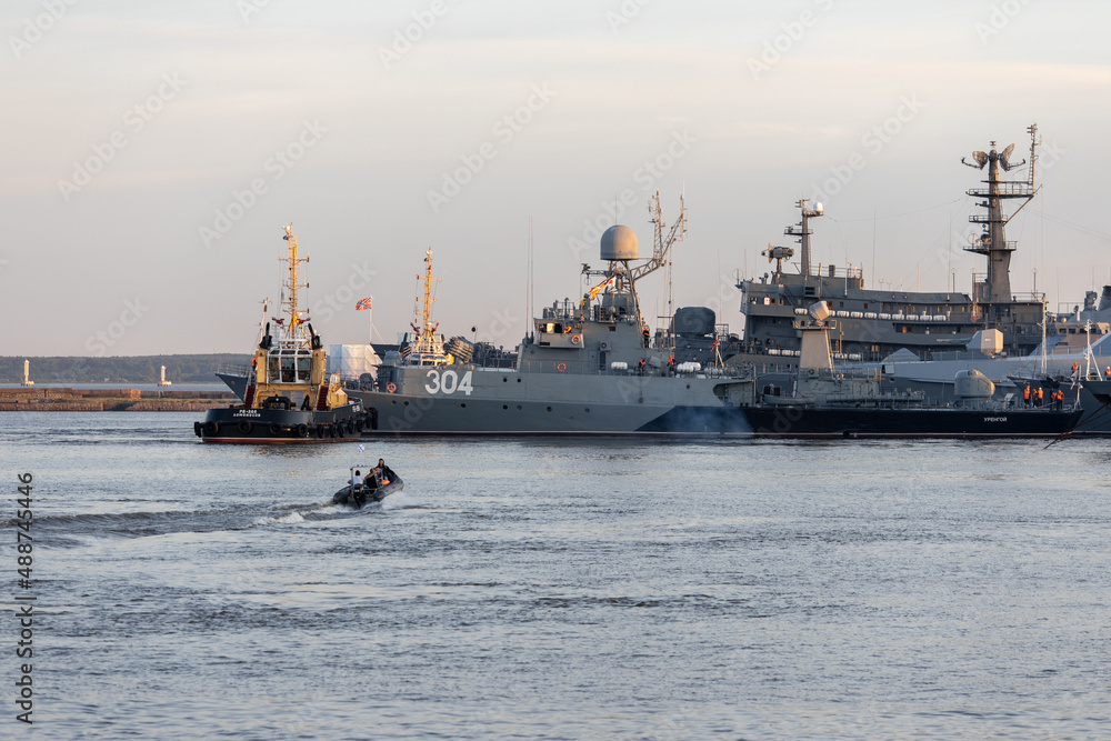 A tug and a rubber boat with sailors at the Petrovskaya pier in the city of Kronstadt against the backdrop of warships. Evening sunset. Two harbor tugs of the Navy. Russia, Kronstadt, July 26, 2020.