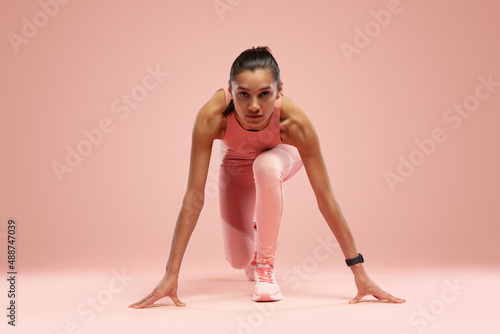 Fototapeta Naklejka Na Ścianę i Meble -  Fit young woman standing in start position over pink background. Sportswoman about to start a run