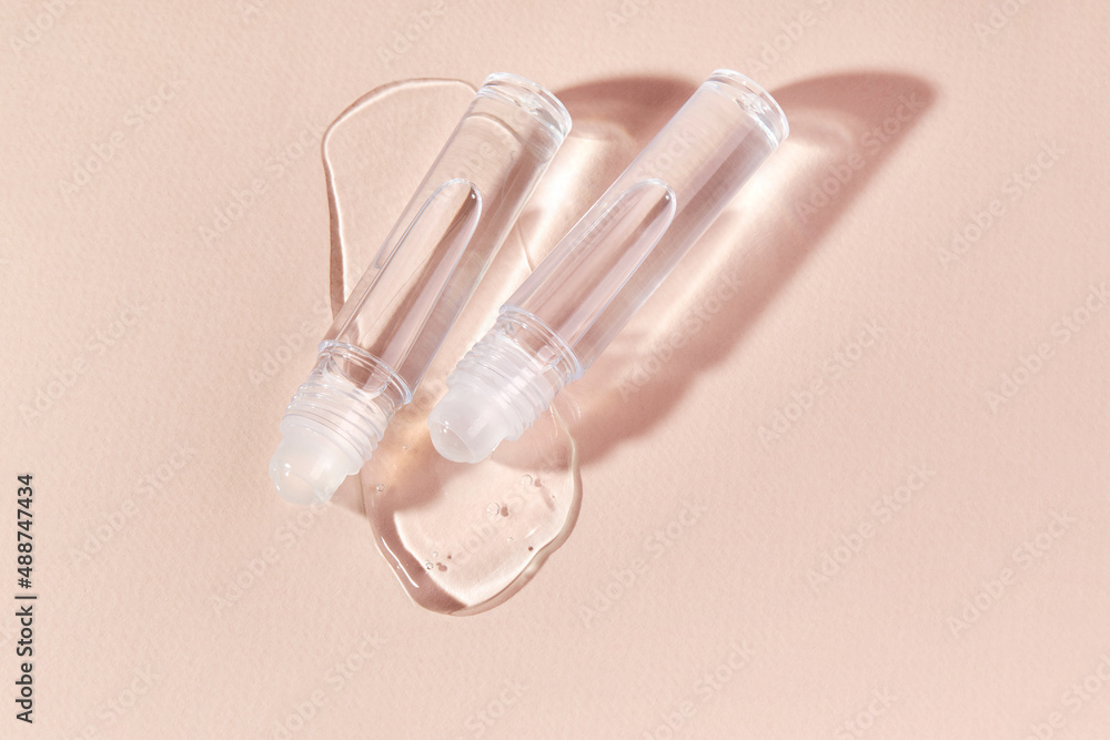 Transparent lip gloss in a roller ball bottles on a beige background. Decorative cosmetic lipstick. Beauty makeup product Transparent lip gloss in a roller ball bottles on a beige background. Decorative cosmetic lipstick. Beauty makeup product