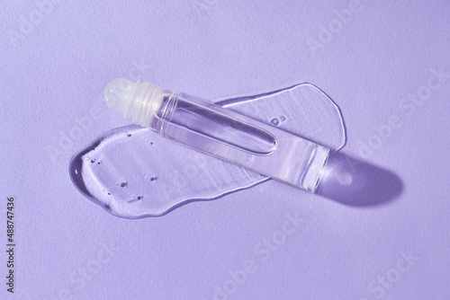 Transparent lip gloss in a roller ball bottles on a purple background. Decorative cosmetic lipstick. Beauty makeup product 