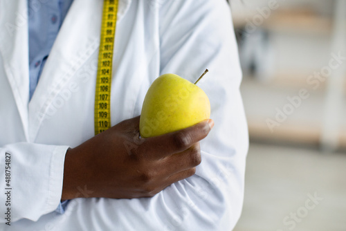 An apple a day and a virus away. Green fresh apple in black female doctor hand, nutritionist posing with measuring tape © Prostock-studio