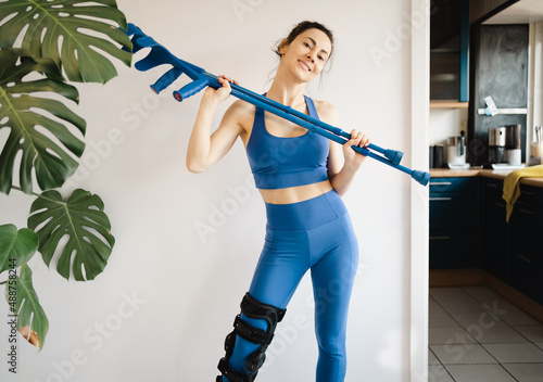 Sportliche Frau hält die Gehhilfen und trägt Orthese