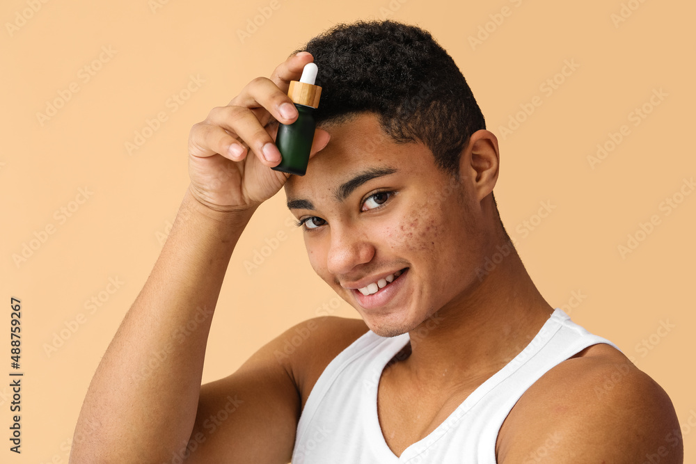 Fototapeta premium Young African-American guy with serum for skin care on color background