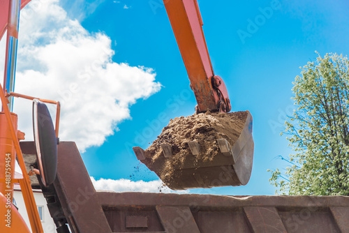Excavation works. The bucket of the tractor loads the soil with a shovel into the back of a dump truck on the construction site