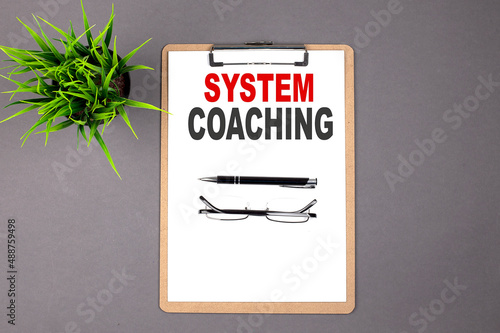 SYSTEM COACHING on the brown clipboard on the grey background. Business concept photo