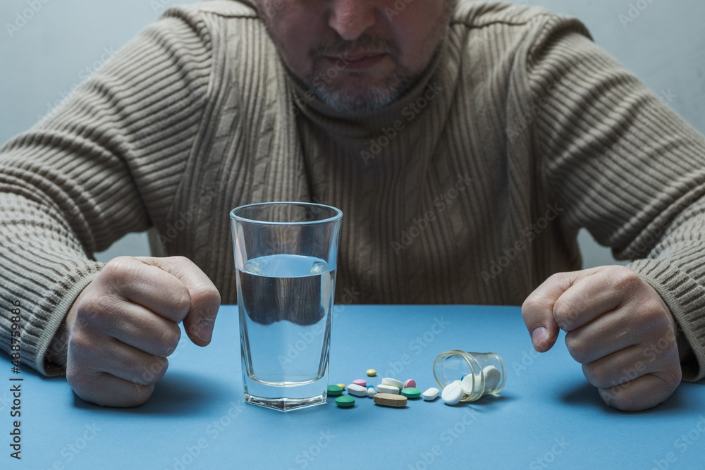 Man clenches his hands into fists, medical preparations and a glass of water are on the table in front of him. Man clenches his hands into fists, medical preparations and a glass of water are on the table in front of him.