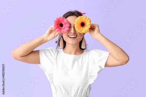 Young woman closing eyes with gerbera flowers on violet background. International Women's Day photo