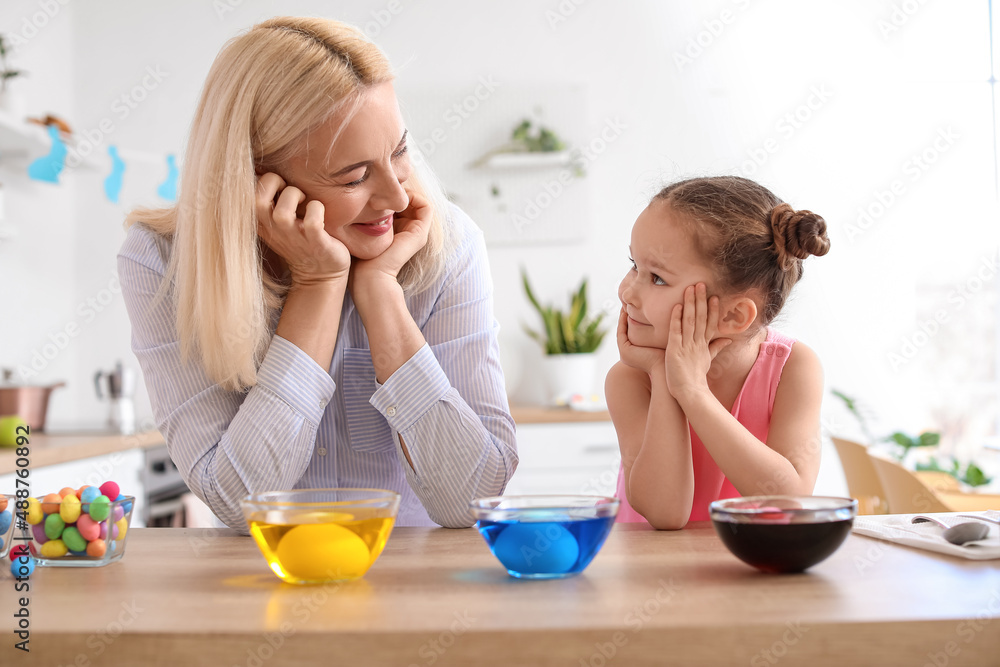 Little girl and her grandmother painting Easter eggs at home