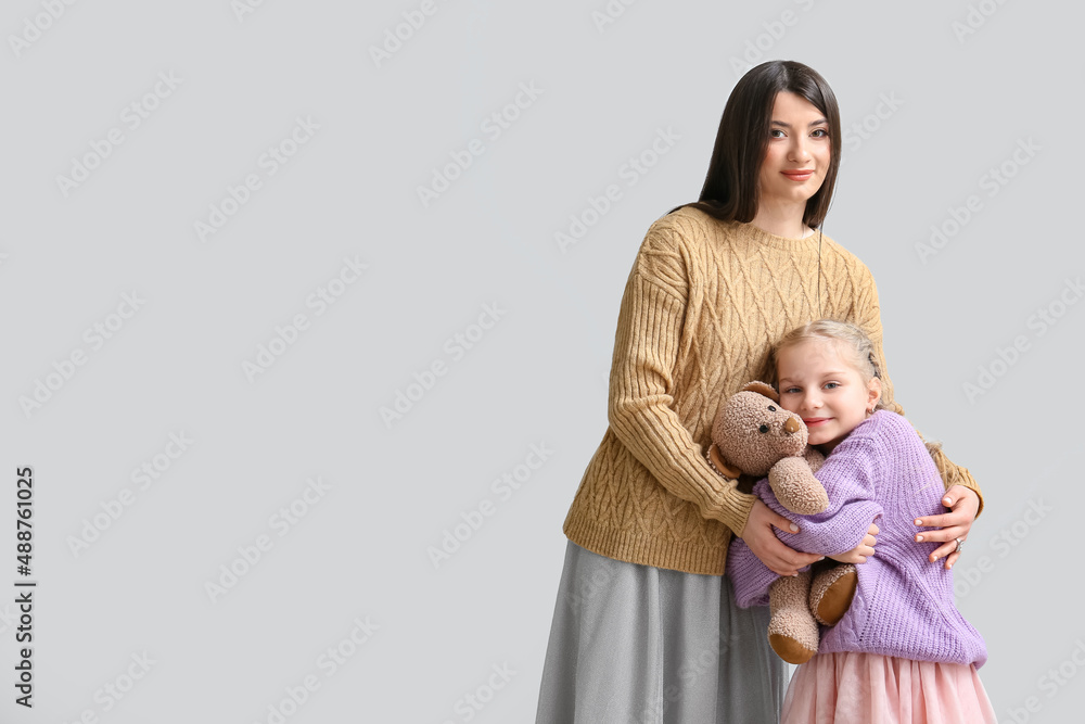 Little girl with toy and her mother in warm sweaters on light background