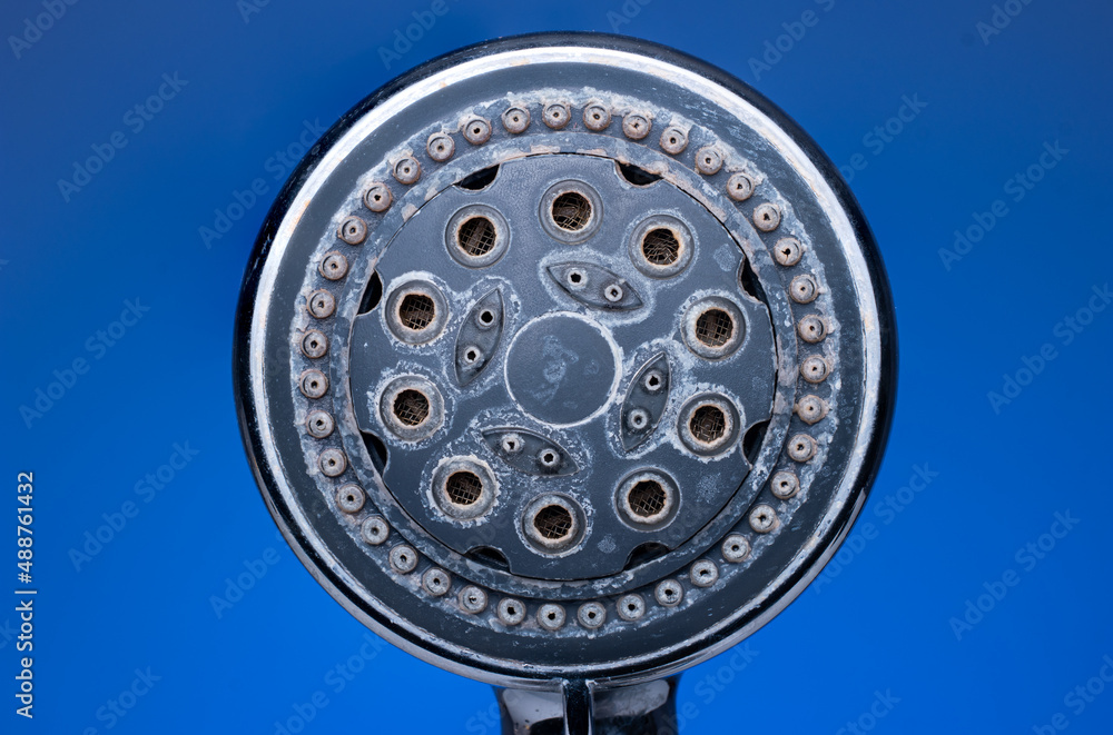 Silver metal shower head with hard water damage or lime scale calcium deposits. Close up studio macro shot, isolated on blue background Silver metal shower head with hard water damage or lime scale calcium deposits. Close up studio macro shot, isolated on blue background