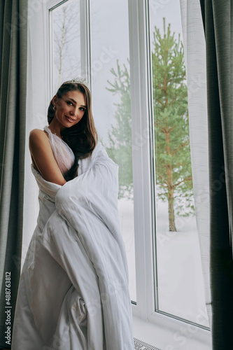 a woman looks out the window, wrapped in a blanket