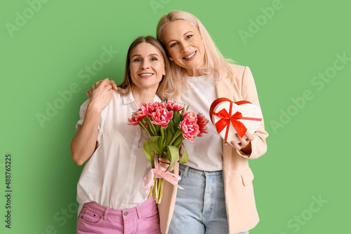 Young woman with her mother and gifts on green background. International Women's Day