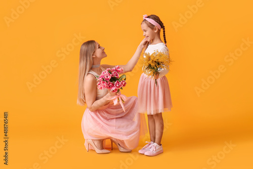 Little girl with her mother and flowers on yellow background