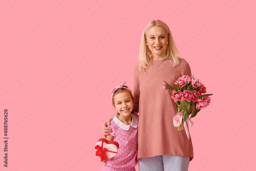 Little girl with her grandmother and gifts on pink background. International Women's Day Little girl with her grandmother and gifts on pink background. International Women's Day