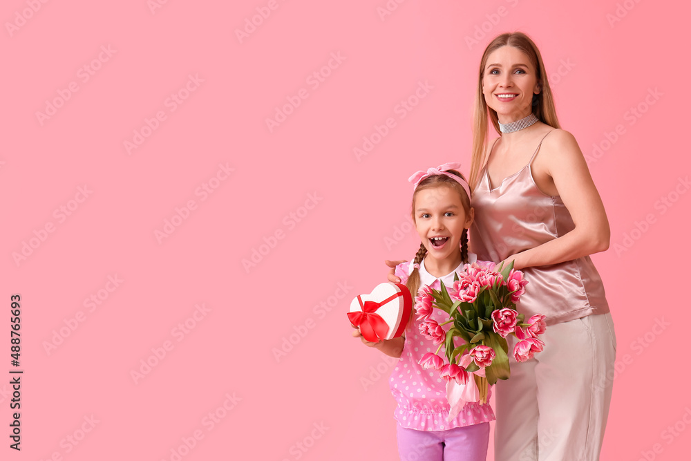 Little girl, her mother with tulips and gift on pink background