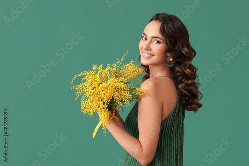Smiling young woman with mimosa flowers on green background. International Women\'s Day