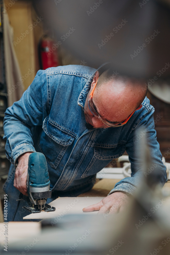 Man with jigsaw sawing wooden plate in workshop