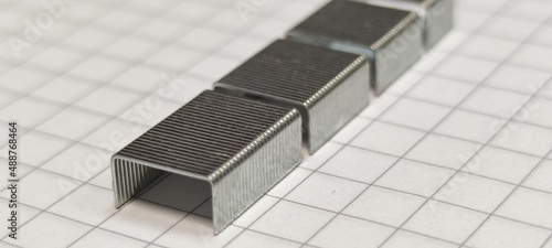 Metal staples on a notebook sheet. On a large checkered notebook sheet are metal shiny staples for a stapler. Staples are connected in small blocks. photo