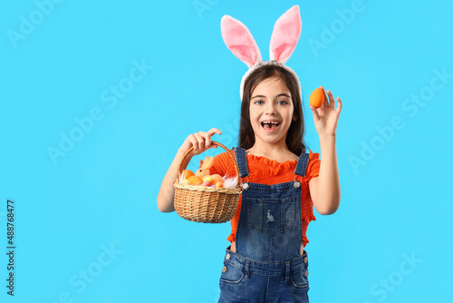 Canvas Print Cute little girl with bunny ears and Easter basket on blue background
