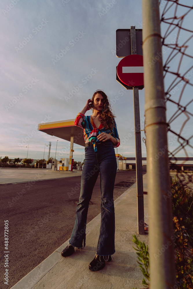 Chica delgada de pelo ondulado poniéndose botas y tomándose fotos en gasolinera