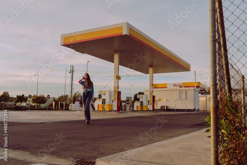 Chica delgada de pelo ondulado poniéndose botas y tomándose fotos en gasolinera