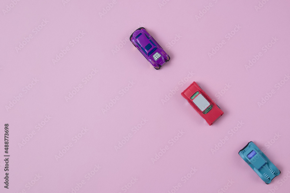 Cars of different colors go one after the other on a pink background with copy space. Minimalistic flat lay scene. Cars of different colors go one after the other on a pink background with copy space. Minimalistic flat lay scene.