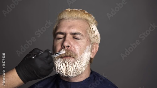 Hairdresser colorist dyes the mustache hair of a bearded man. Hair salon, hair coloring man. Attractive senior barber doing a haircut and haircolor for client at barber shop.