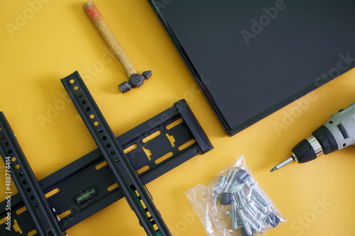 Canvas Print Bracket for wall mounting computer monitor or TV, electric drill-driver, mounting screws and TV screen on yellow background