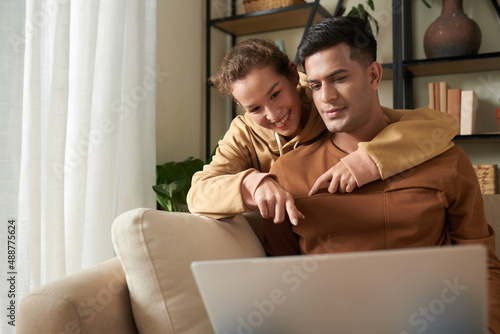 Young happy woman pointing at laptop and choosing the things online together with her boyfriend during their online shopping © DragonImages