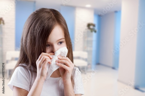 Young kid feels unwell, blows nose in tissue, suffers from running nose, cold symptoms or allergy