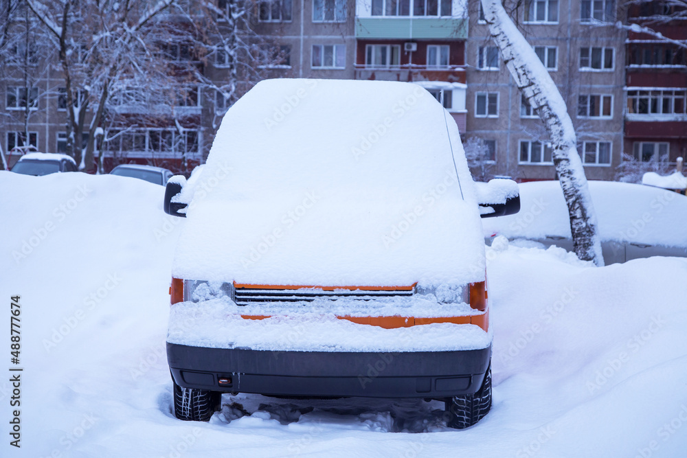Orange car, van covered snow after snowfall and blizzard on town street in winter Orange car, van covered snow after snowfall and blizzard on town street in winter