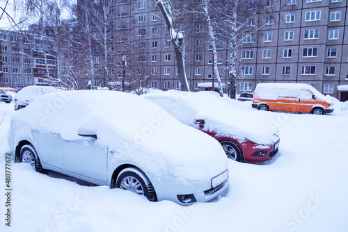 Cars on parking covered snow in snowbank after snowfall and blizzard in winter