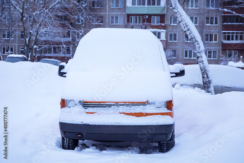 Orange car, van covered snow after snowfall and blizzard on town street in winter