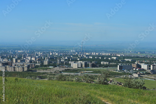 view of the city landscape in central asia in spring with pipes and with grass in the foreground and blue sky
