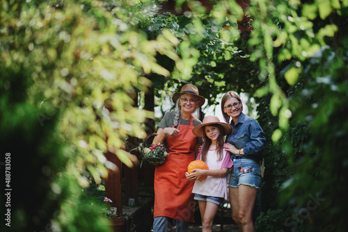 Happy little farmer girl with mother and grandmother looking at camera outdoors at garden