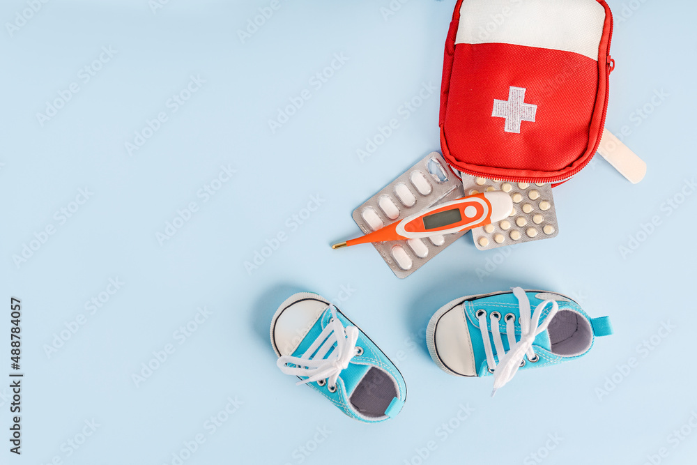 Children's shoes and a first aid kit with a thermometer and pills on a blue background. Space for text. The concept of children's health, treatment