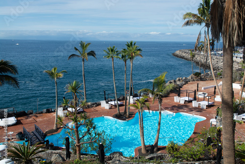 Beach club with blue swimming pool and palm trees on coast of Atlantic ocean, Costa Adeje, Tenerife, Spain