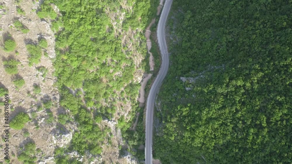 Aerial top view of traffic road surrounded by forest between the mountains